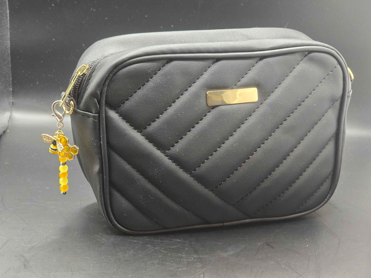 Gray quilted bag with a bee themed zipper charm hanging from the zip