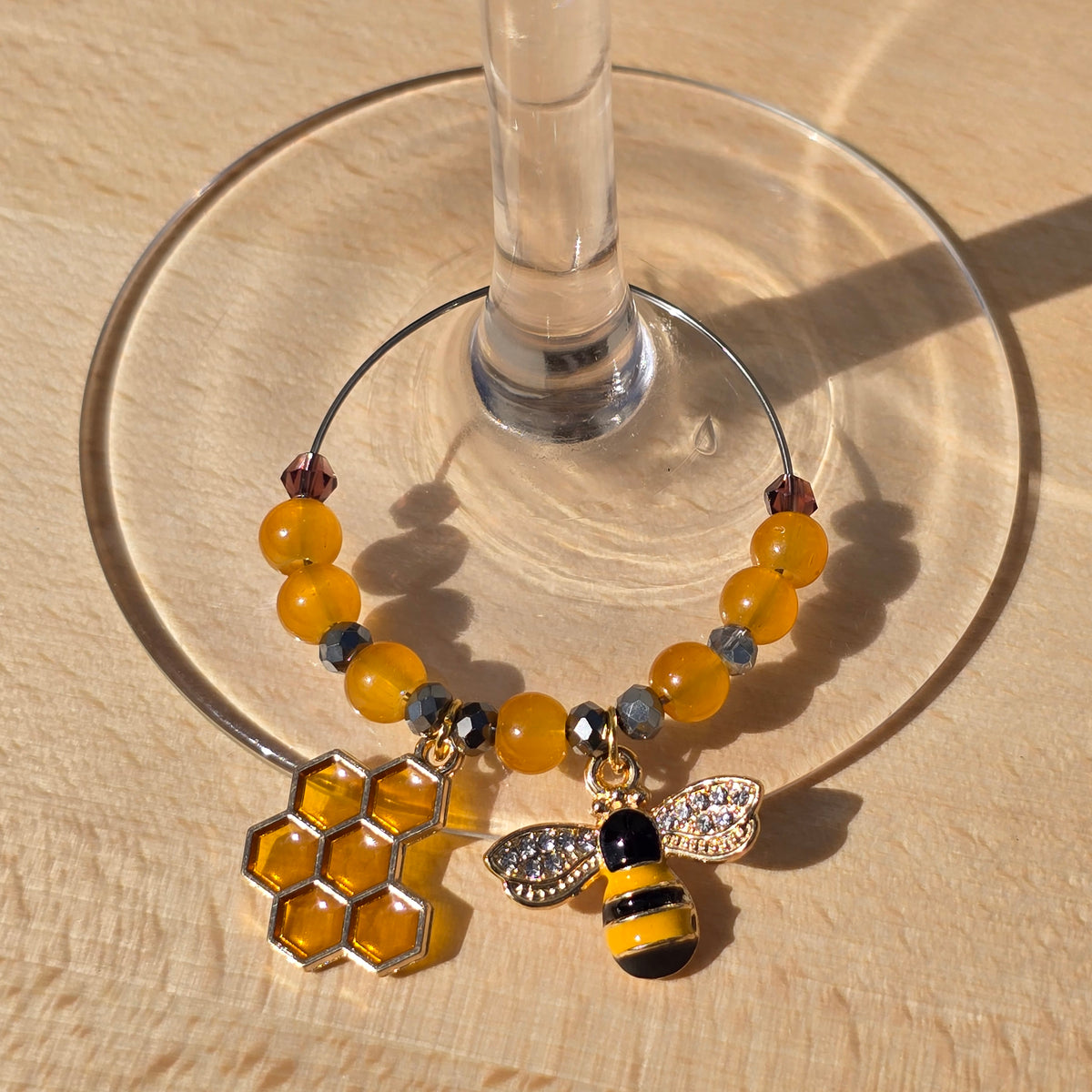lifestyle shot of a wine glass charm with a bee theme clipped onto the base of a glass stem