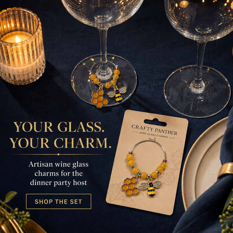 Two beaded wine glass charms with yellow honeycomb and bumblebee details are displayed on a dark navy tablecloth with wine glasses, plates, and a lit candle. One charm is shown on a card labeled 'Crafty Panther Mini Glass Charms' and the other is draped over a glass base.