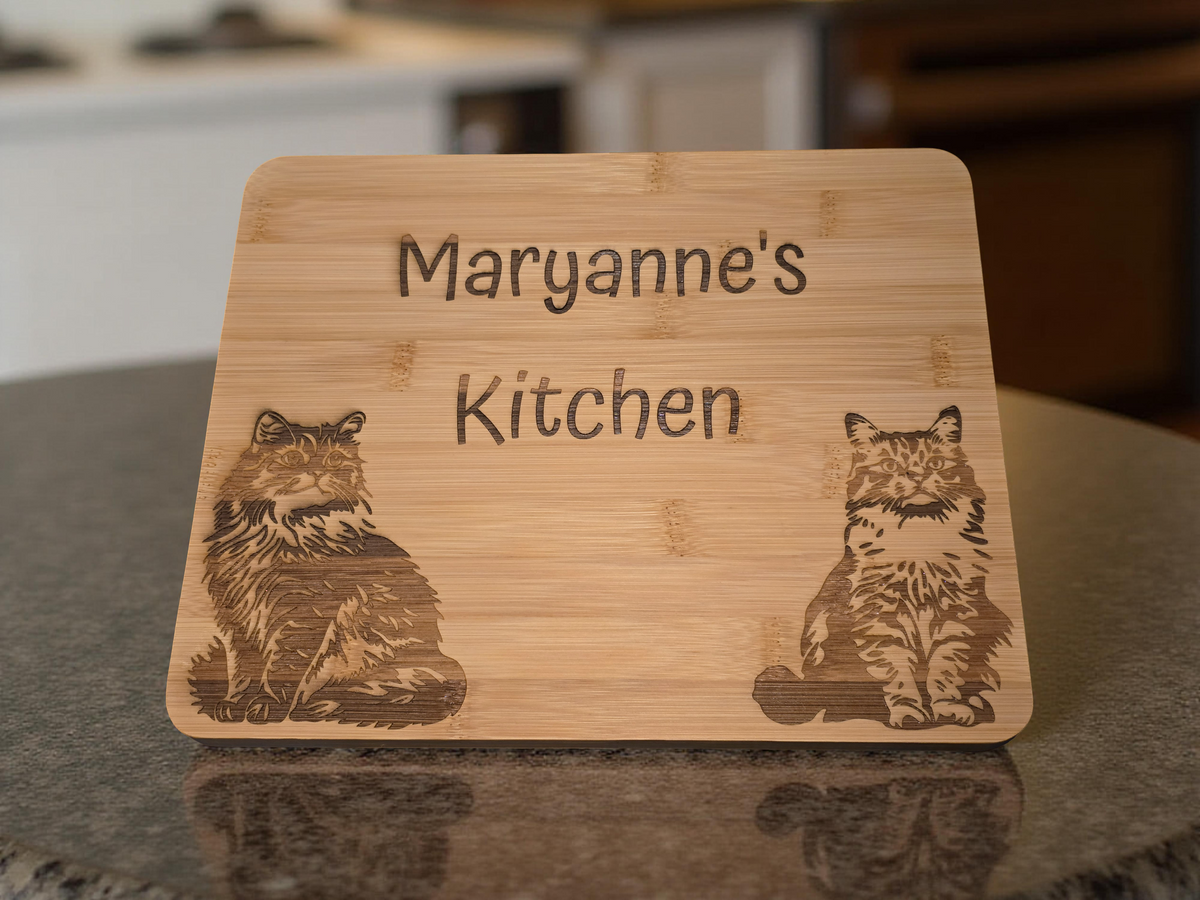 Bamboo cutting board with engraved cat illustrations and personalised text on a kitchen counter.
