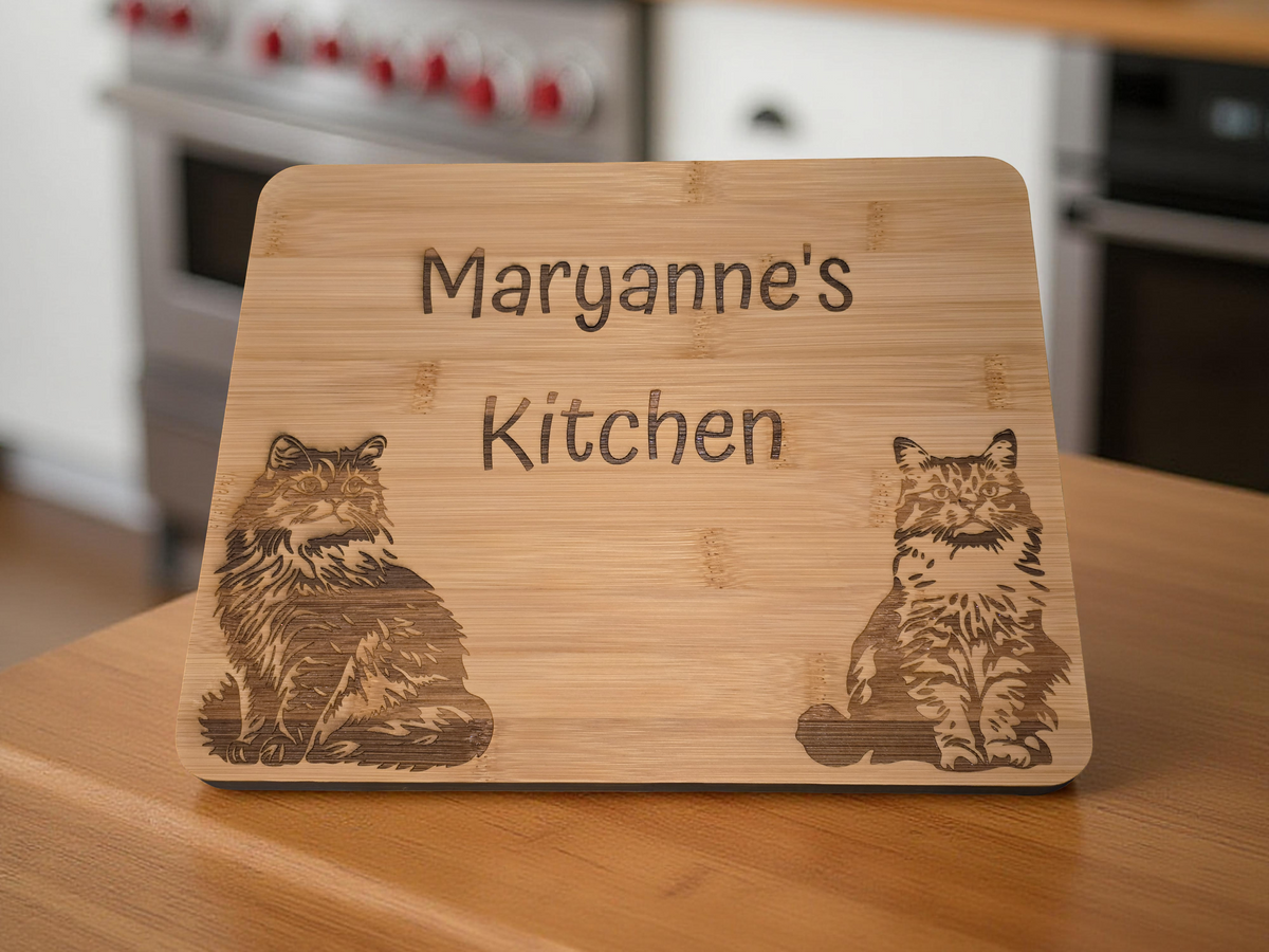 Bamboo cutting board with engraved cat designs and personalised name text on a kitchen counter.