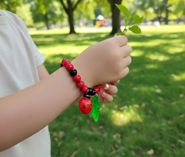 Child wearing a red and black beaded bracelet with a ladybird and green leaf charm in a park setting