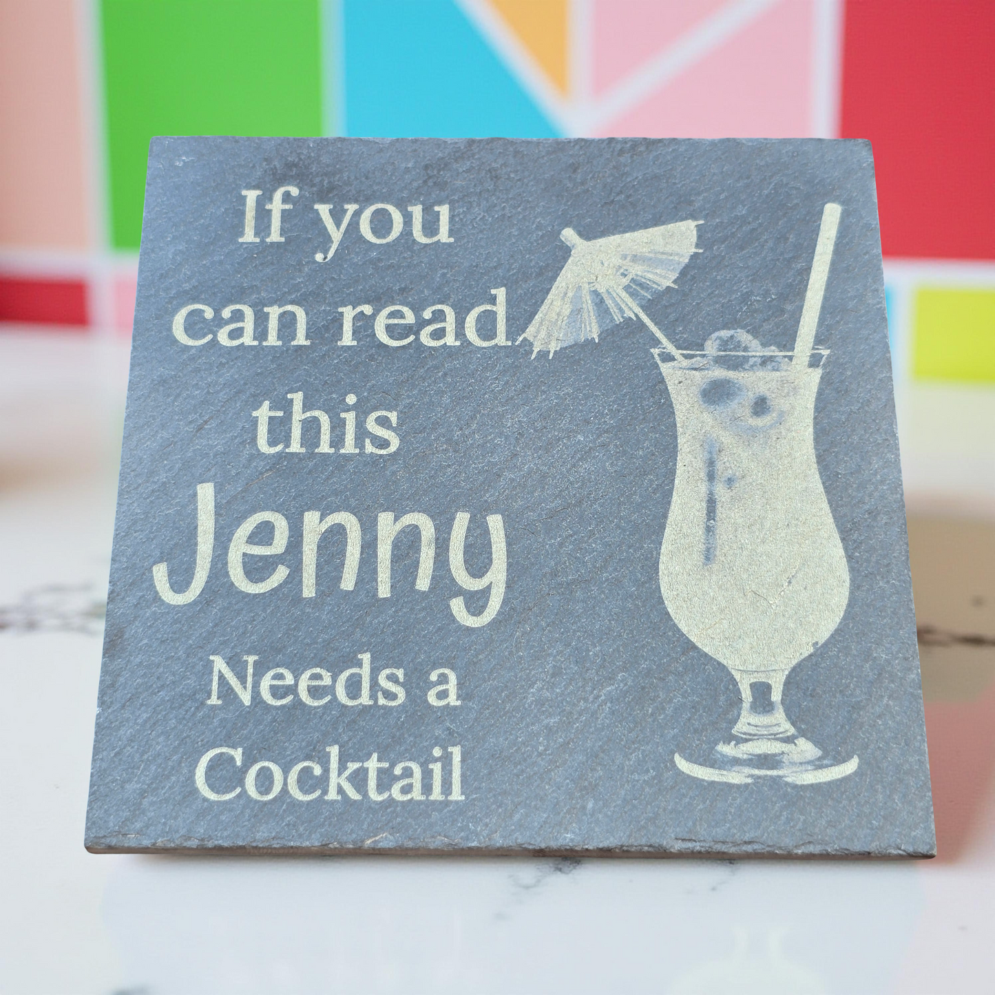 Slate coaster with a drink illustration and text 'If you can read this Jenny Needs a Cocktail' on a colorful background.