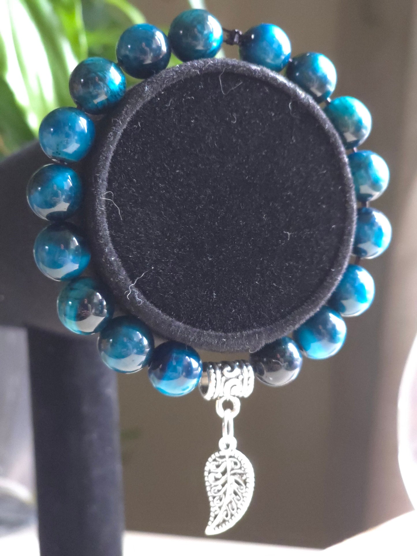 Blue glass beaded bracelet with a silver leaf dangle charm on a bracelet display stand