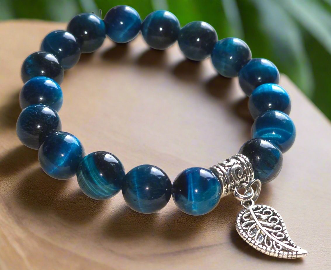 A blue beaded elastic bracelet with a leaf charm, displayed on a wooden surface.
