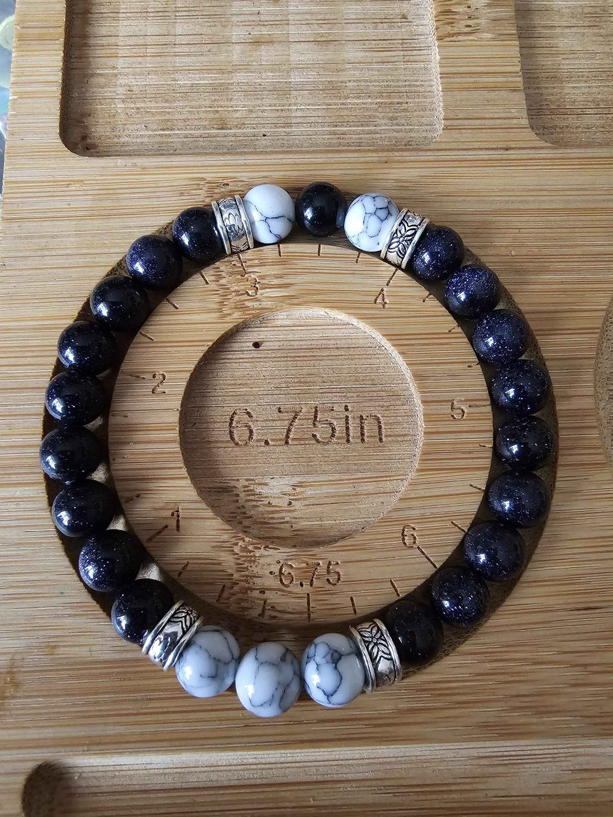 Beaded bracelet with black and white stones on a wooden board with measurement markings showing 6.75inch size