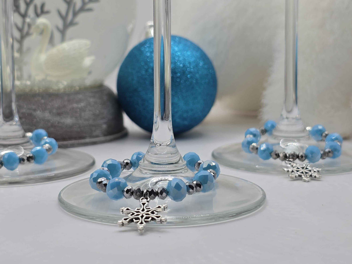 Blue and silver beaded wine glass charms with snowflake pendants wrapped around the stems of wine glasses.