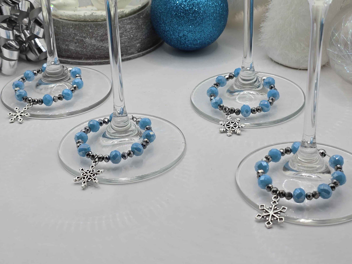 Four wine glass stems decorated with blue and silver beaded charms featuring dangling snowflake pendants.