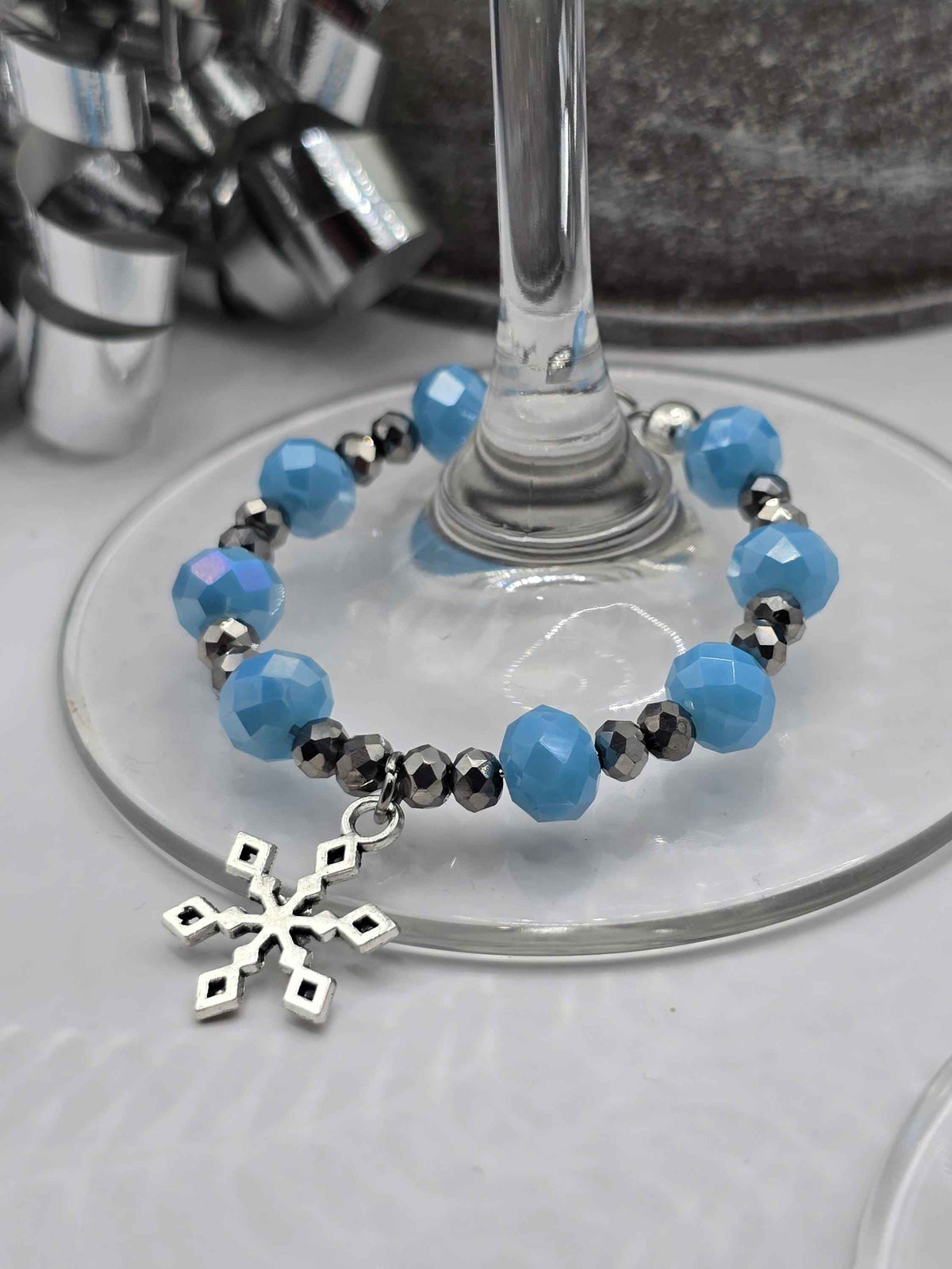 Blue and silver beaded wine glass charm with a dangling snowflake pendant on a wine glass stem.
