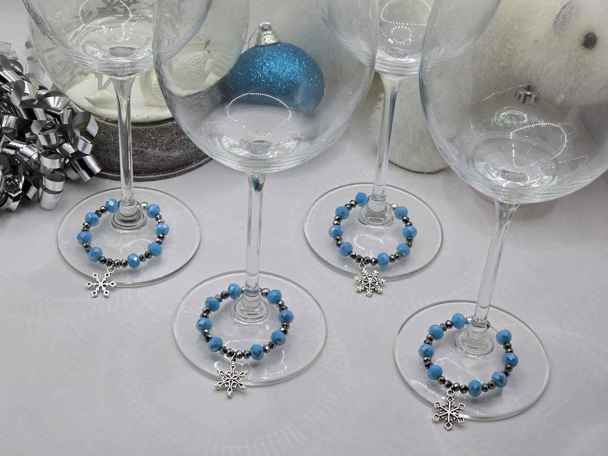 Four wine glasses adorned with light blue and silver beaded charms featuring dangling snowflake pendants.