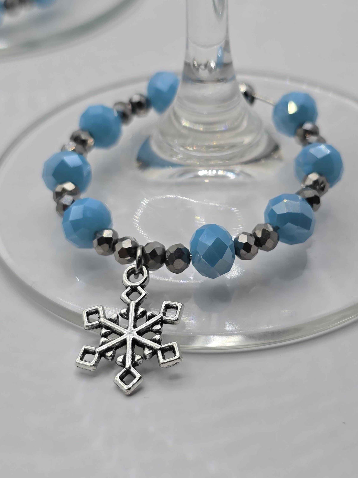 Silver snowflake wine glass charm with faceted light blue and metallic silver beads around a clear glass stem.