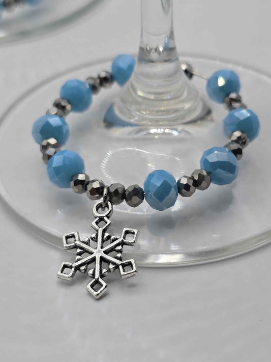 Silver snowflake wine glass charm with faceted light blue and metallic silver beads around a clear glass stem.