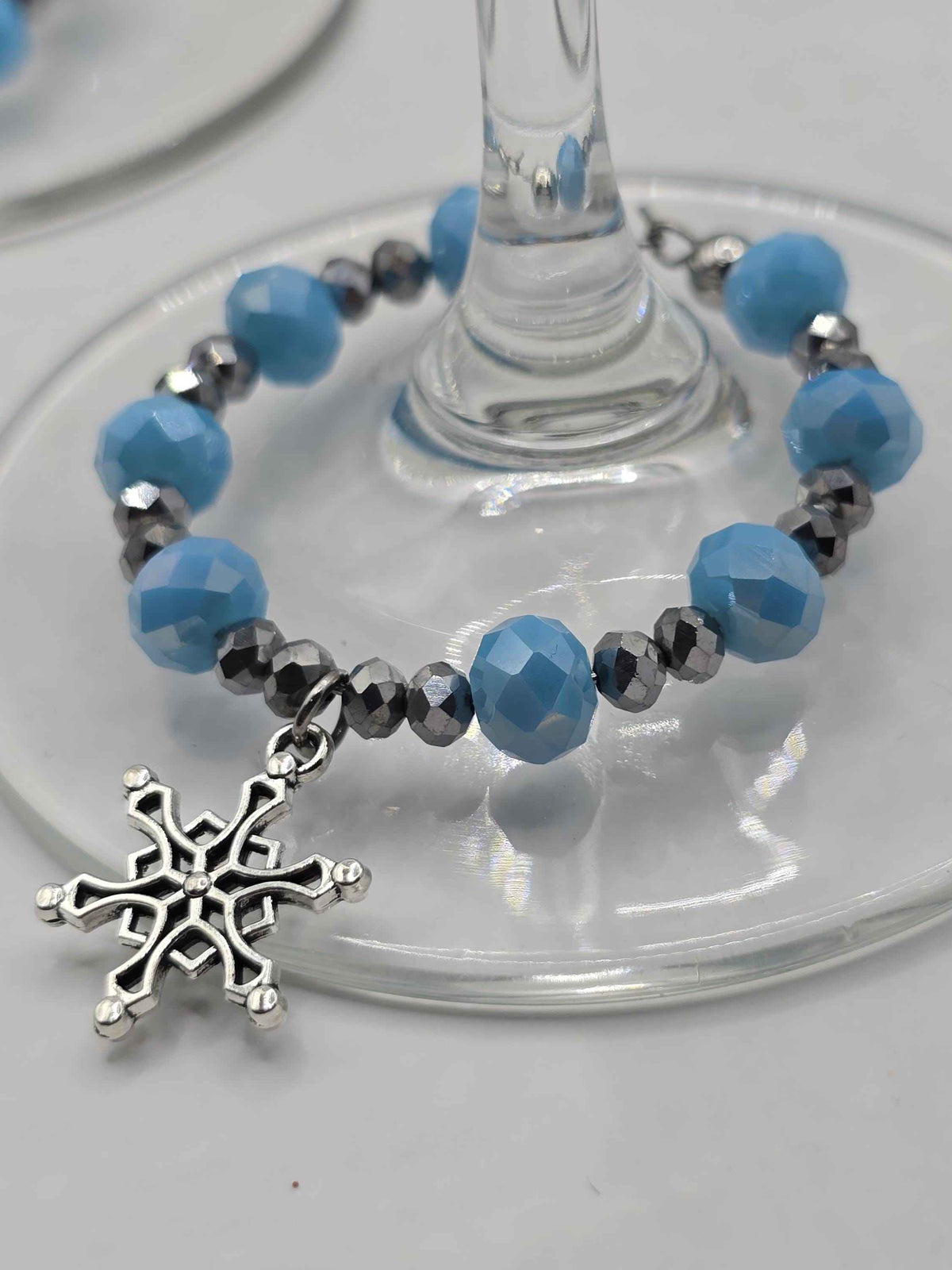 Wine glass charm with faceted blue and silver beads and a silver snowflake pendant wrapped around a glass stem.