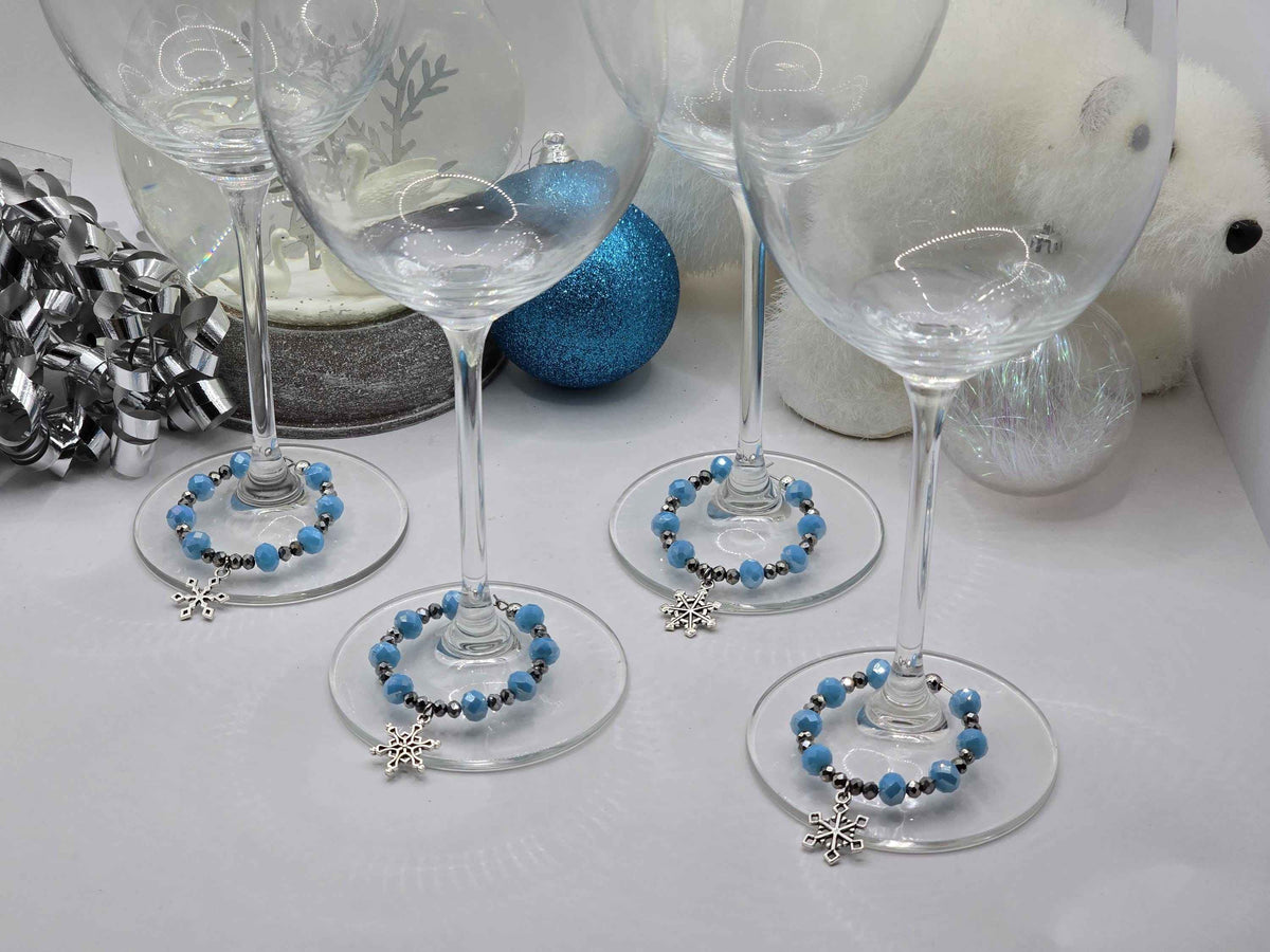 Blue and silver beaded snowflake wine glass charms displayed around the stems of clear wine glasses.