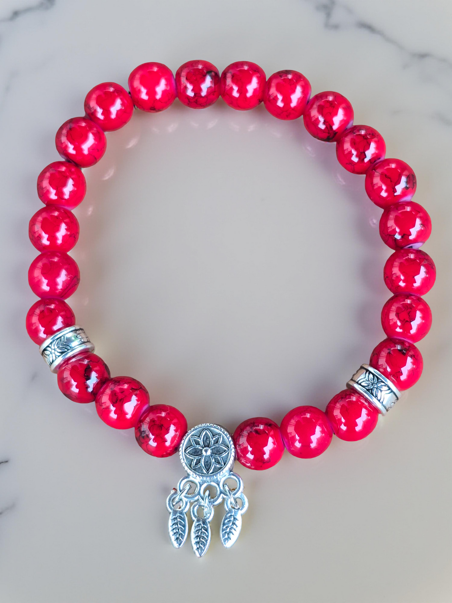 Red beaded bracelet with a silver dreamcatcher charm on a marble surface