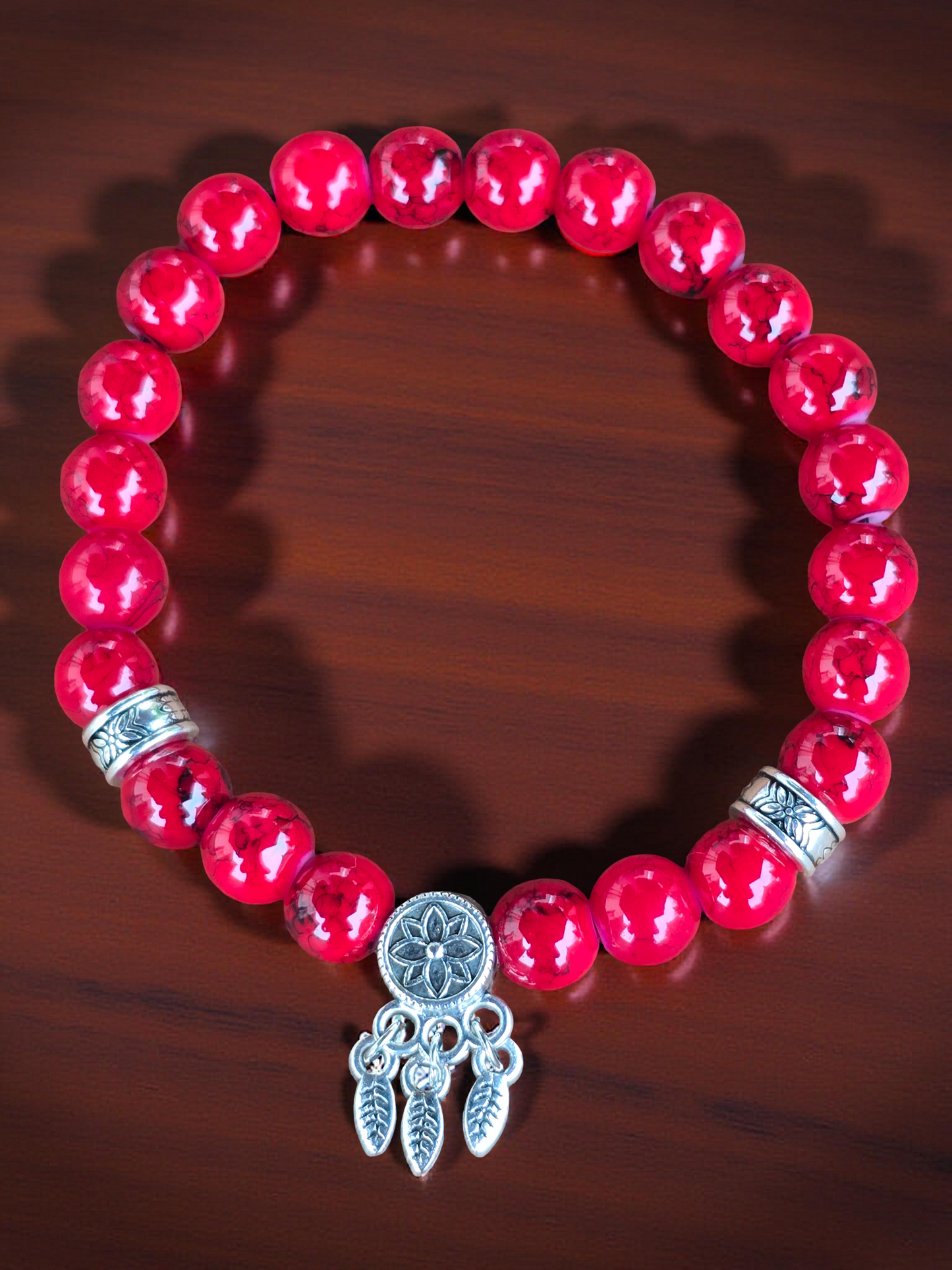Red beaded bracelet with a silver dreamcatcher charm on a wooden surface under bright light