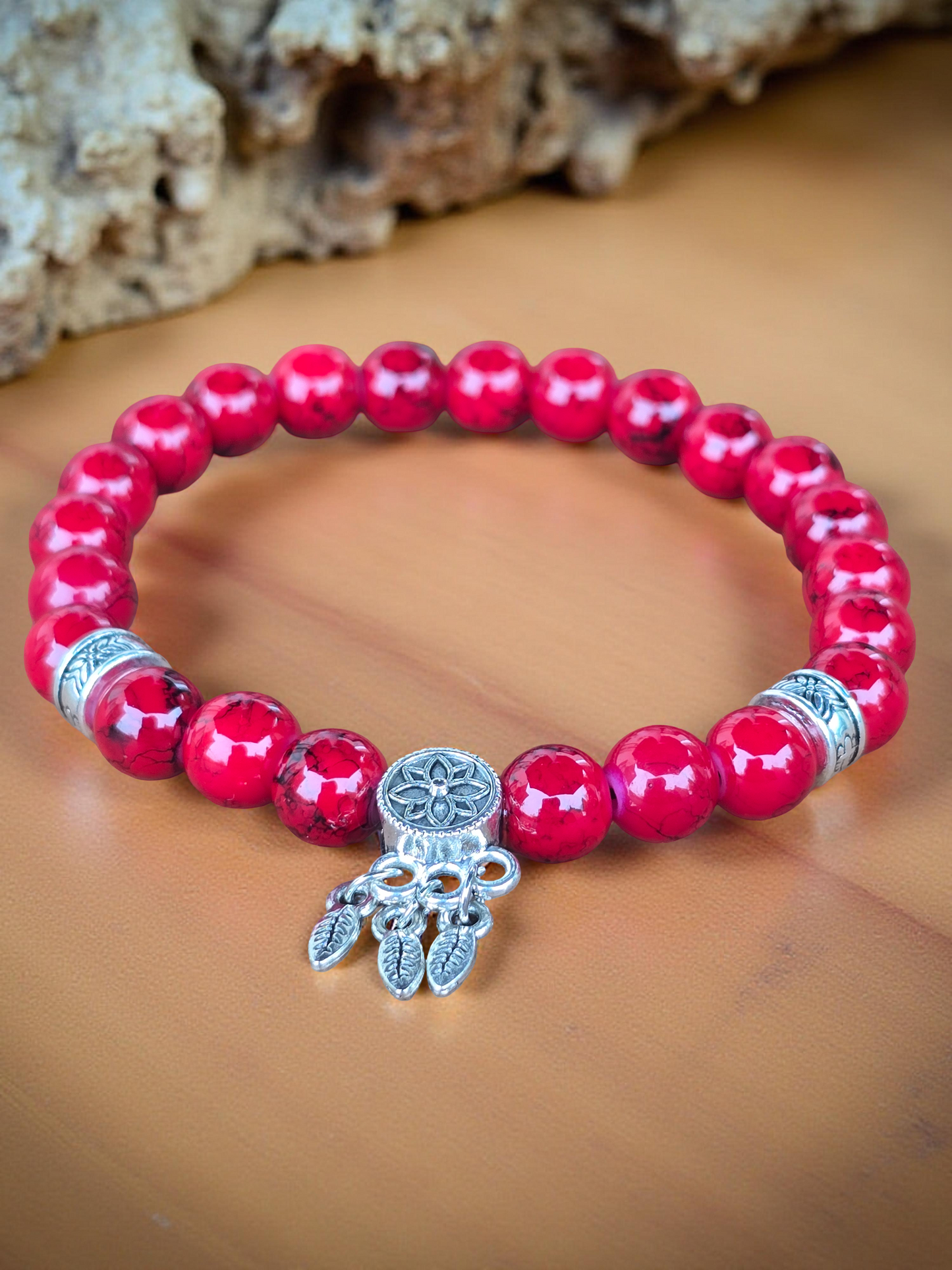 Bright Red beaded bracelet with a silver charm on a wooden surface