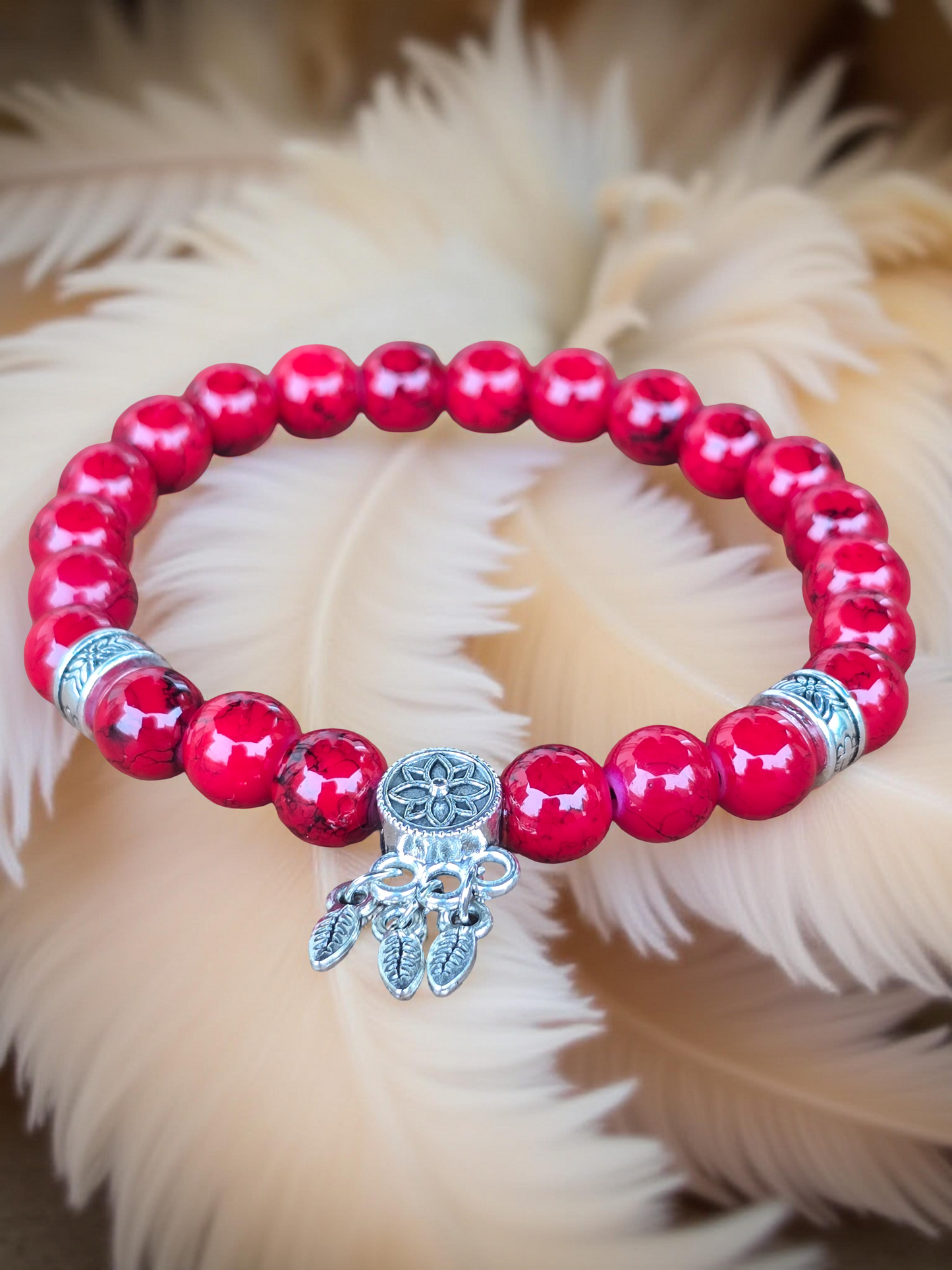Red beaded bracelet with a silver charm on a fluffy beige background