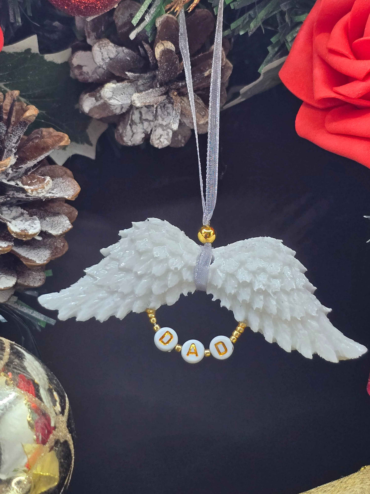 White resin angel wings hanging ornament with a beaded loop below spelling DAD in gold lettering.