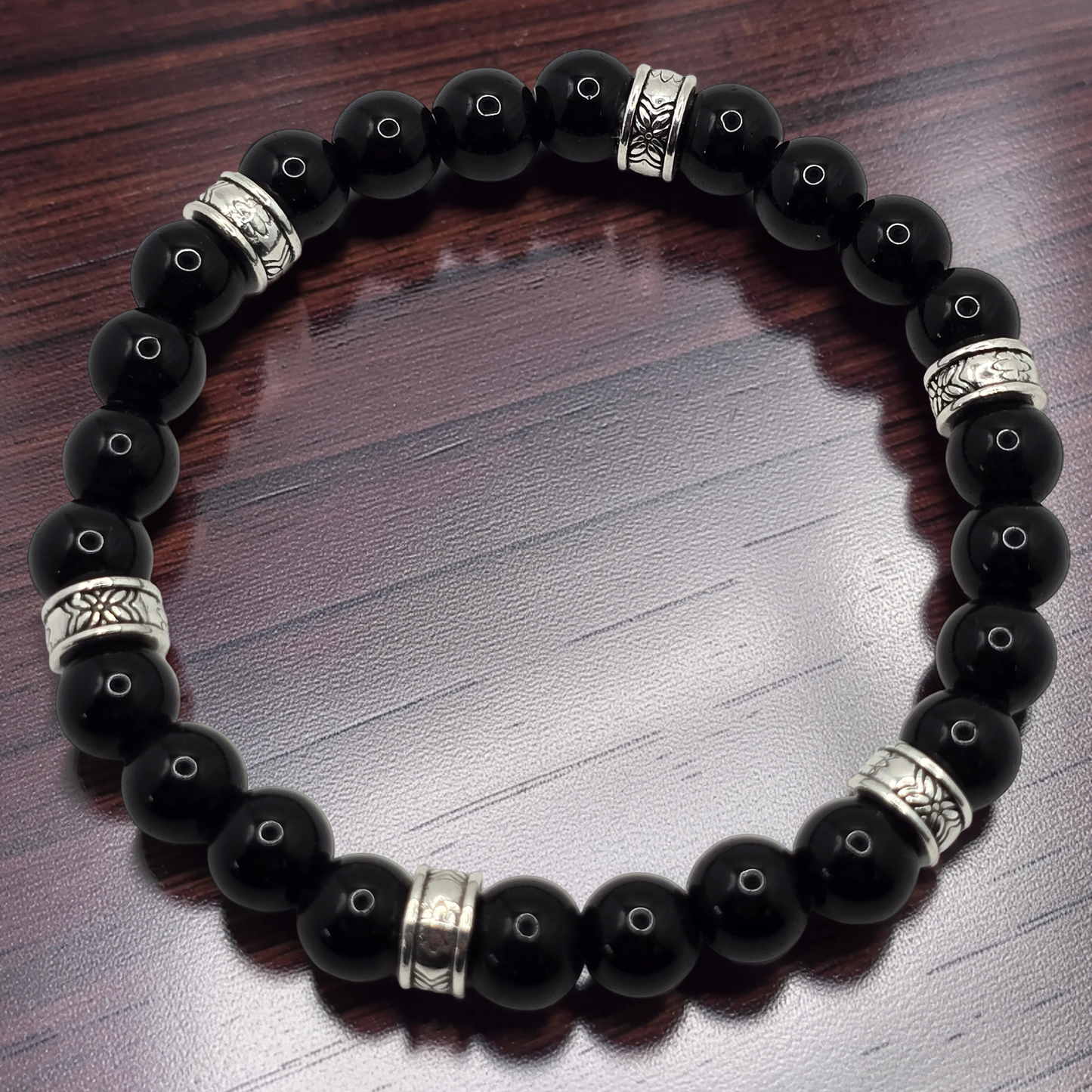 Glossy Black beaded bracelet with silver accents on a wooden surface