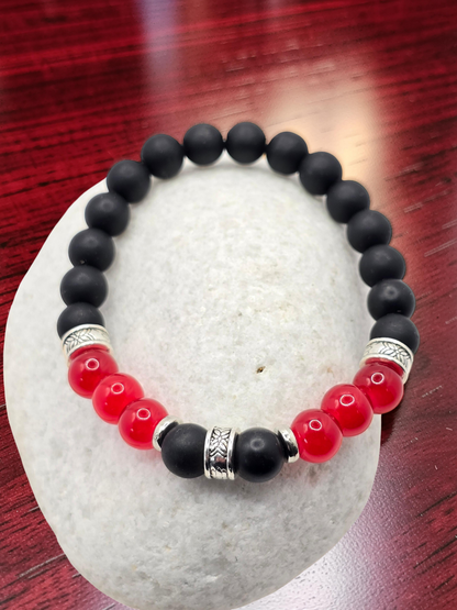 Black and red beaded bracelet with silver accents on a white stone surface.