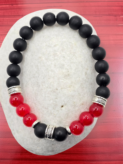 Black and red beaded bracelet with silver accents on a textured white surface.