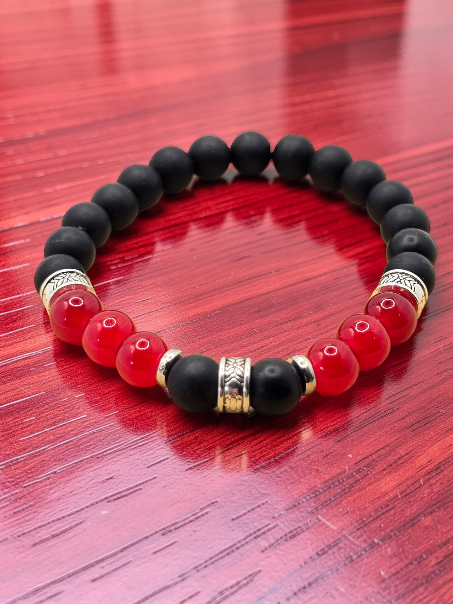 mens Black, red, and gold silver bracelet on a red wooden surface