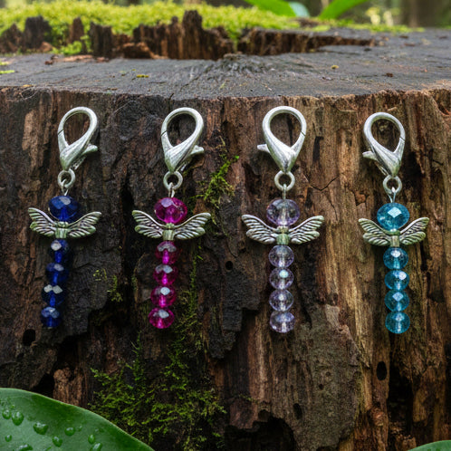Four dragonfly-shaped keychain charms with coloured beads against a wet tree stump