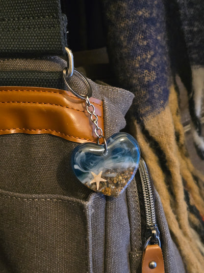 Heart shaped resin keyring with an ocean scene hangs off a bag