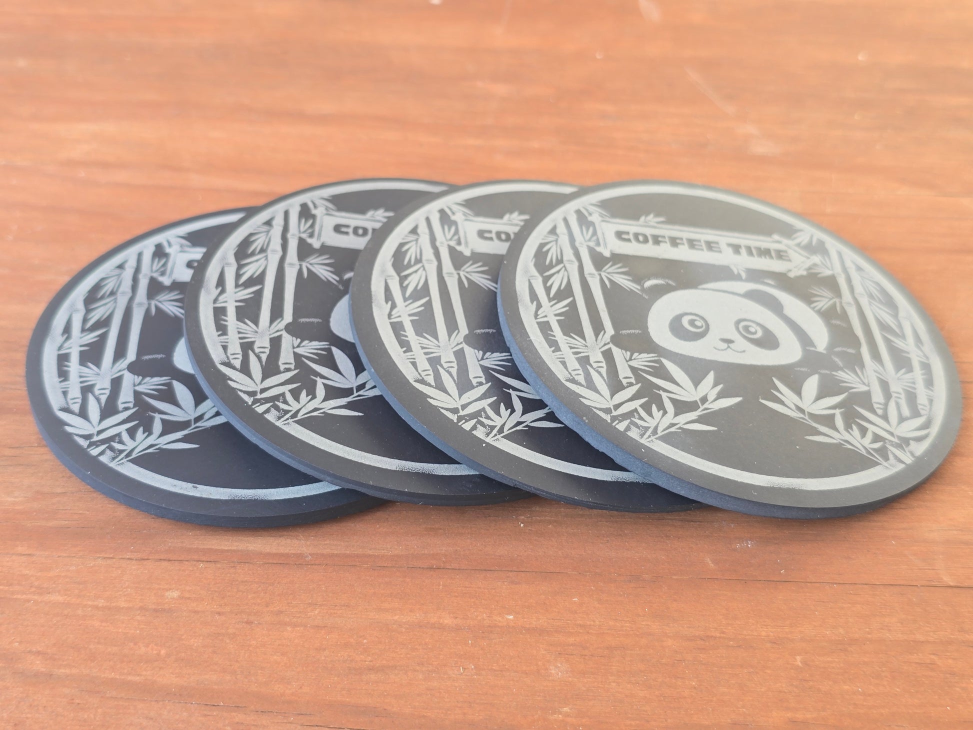 Four black coasters with lying panda and bamboo designs on a wooden surface