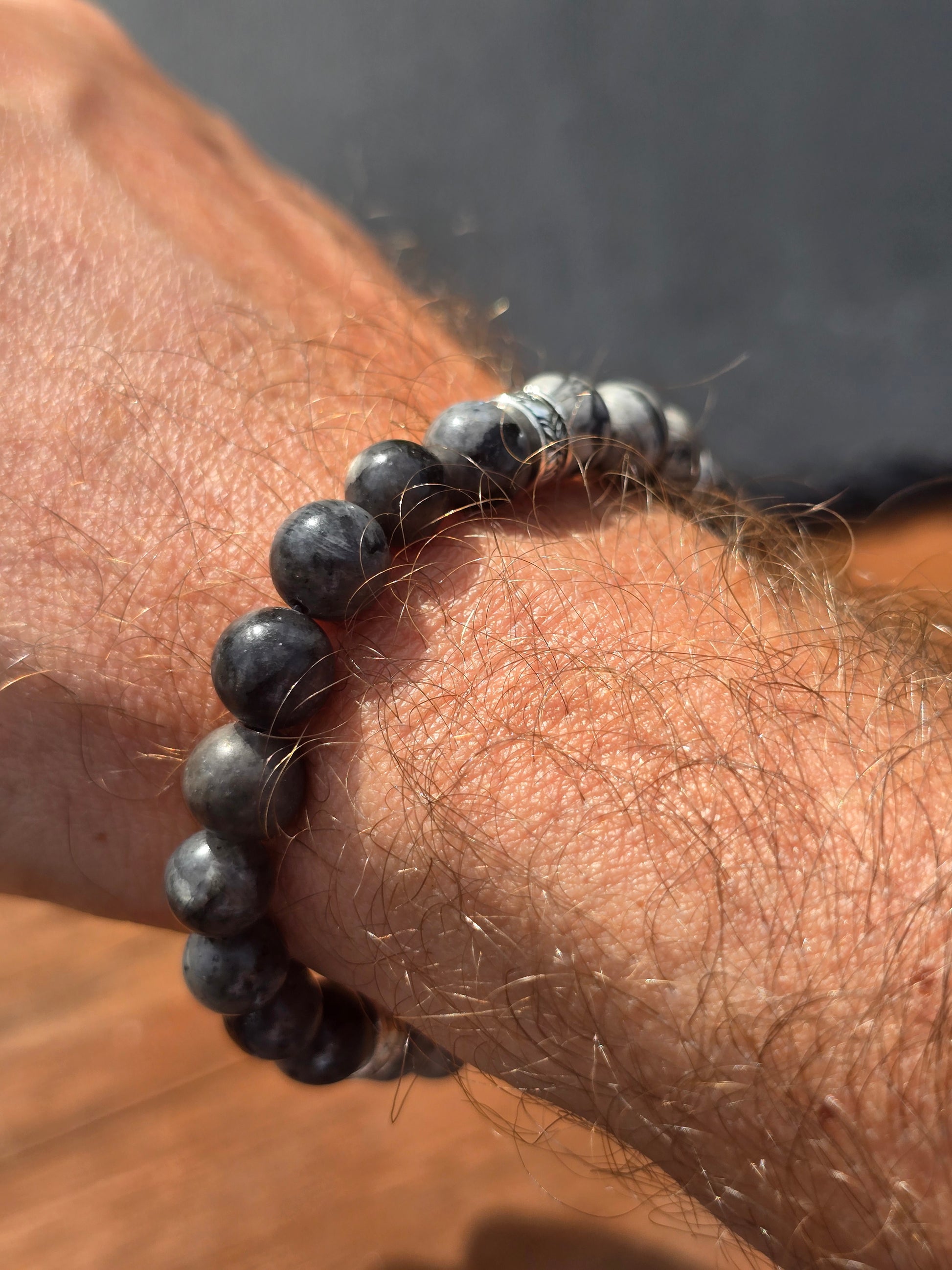 Close-up of a wrist wearing a charcoal grey beaded bracelet against a blurred background