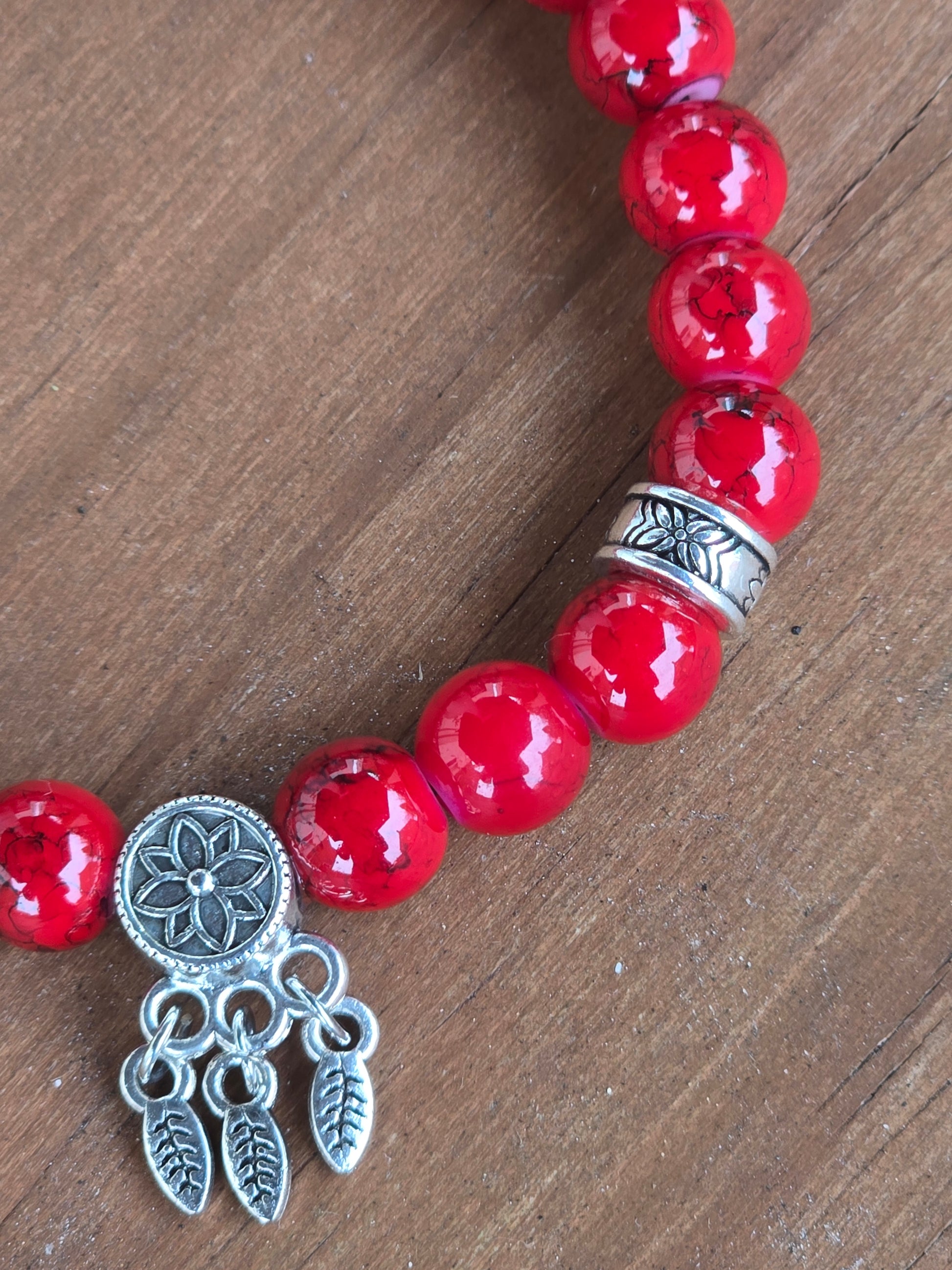 Red beaded bracelet with a silver charm on a wooden surface