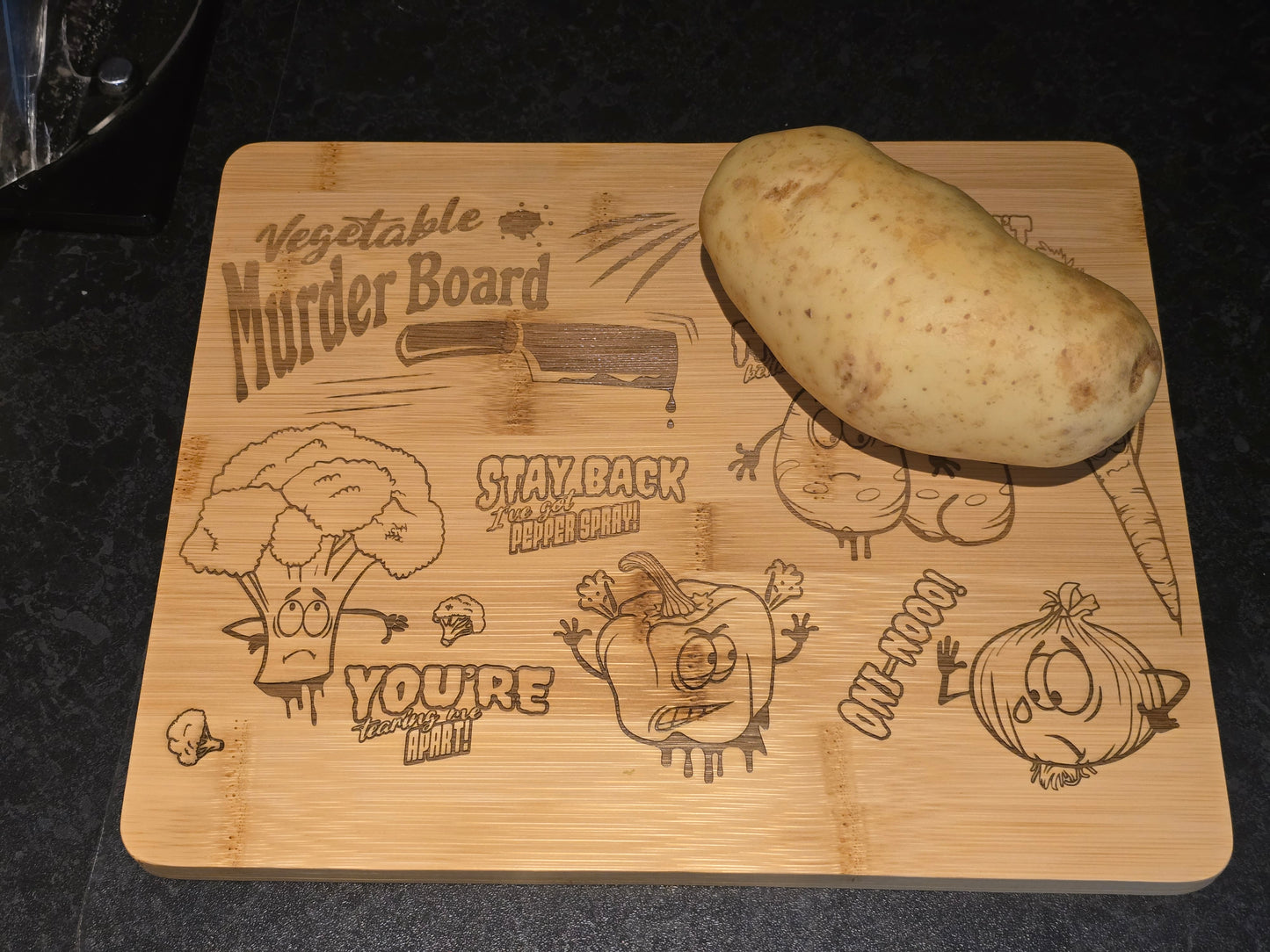 Wooden cutting board with humorous vegetable-themed designs and a potato on top.