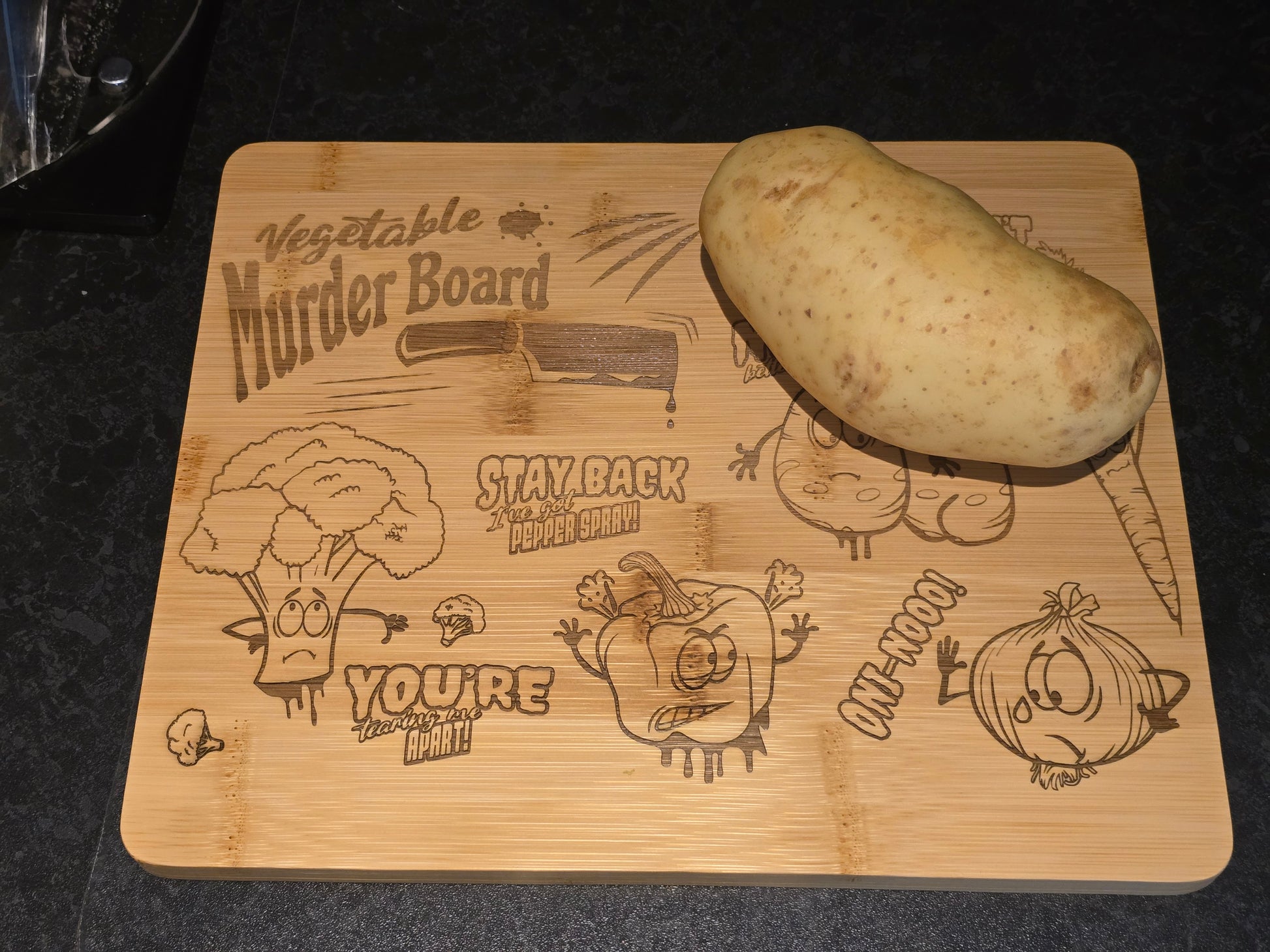 Wooden cutting board with humorous vegetable-themed designs and a potato on top.