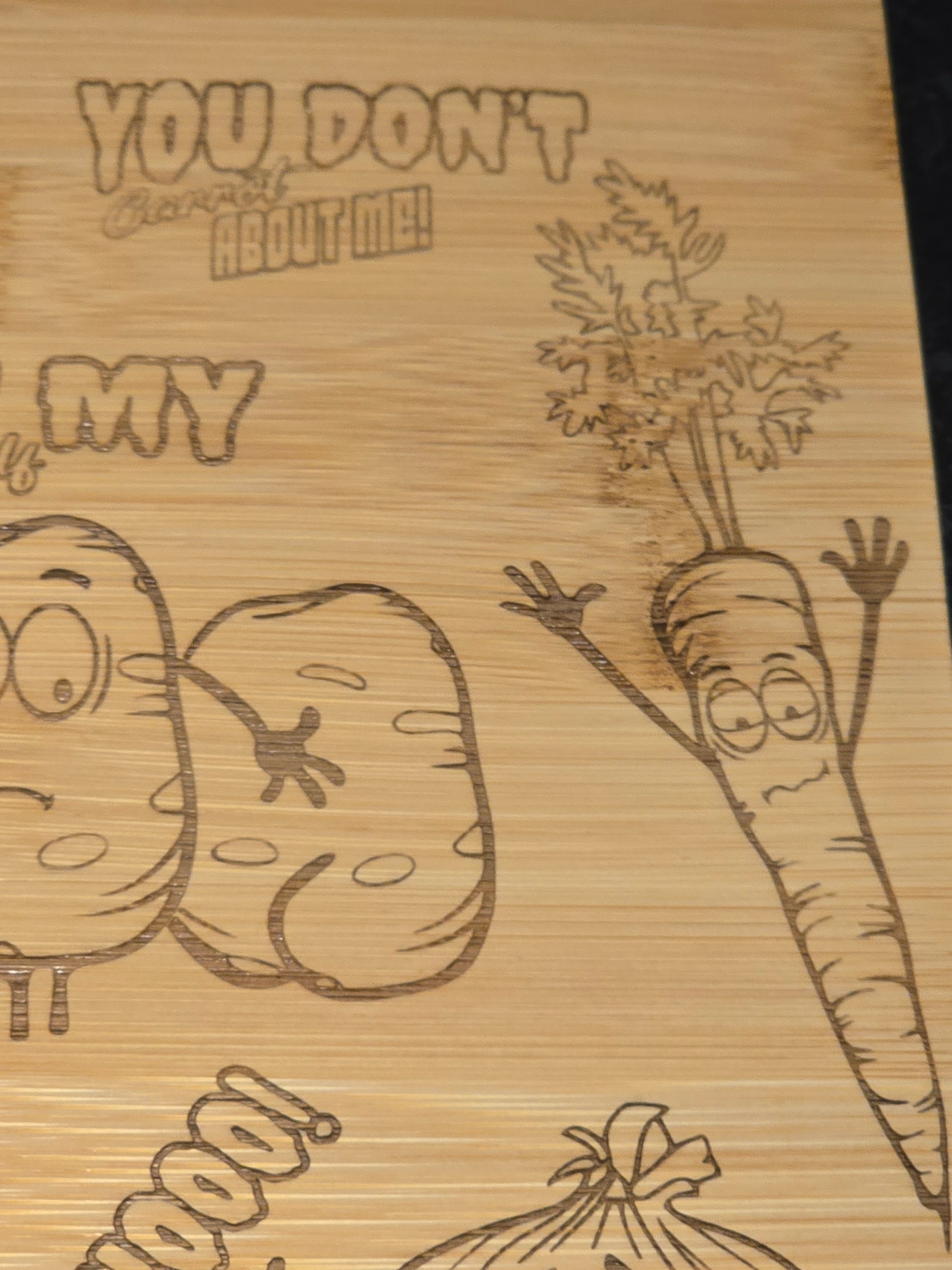 Wooden cutting board with engraved cartoon carrot and potato design.