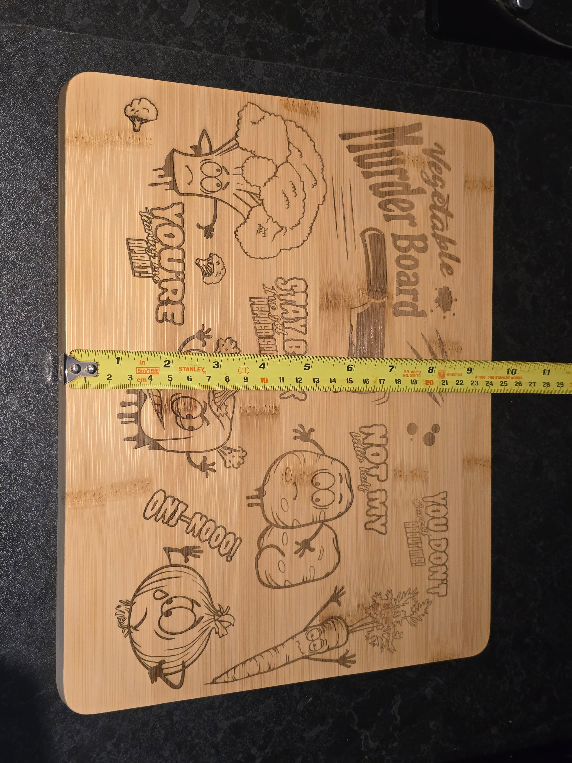 Wooden cutting board with vegetable-themed designs and a measuring tape showing 24cm width
