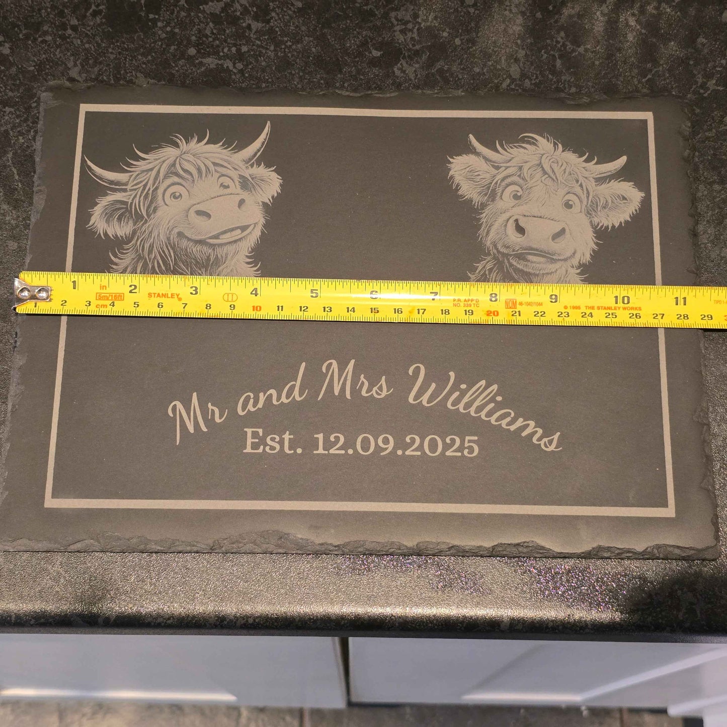 Slate with engraved Highland cow designs and text, measured by a ruler showing 29m length