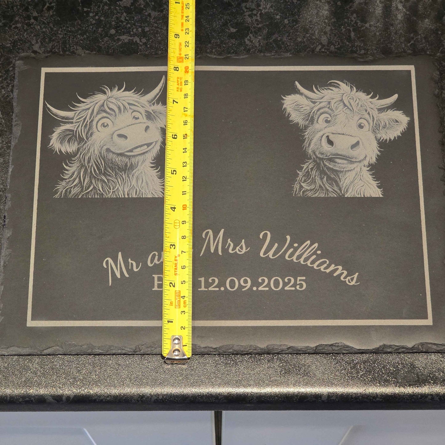 Engraved cheese slate with Highland cow design and text, measured by a tape measure showing 21cm