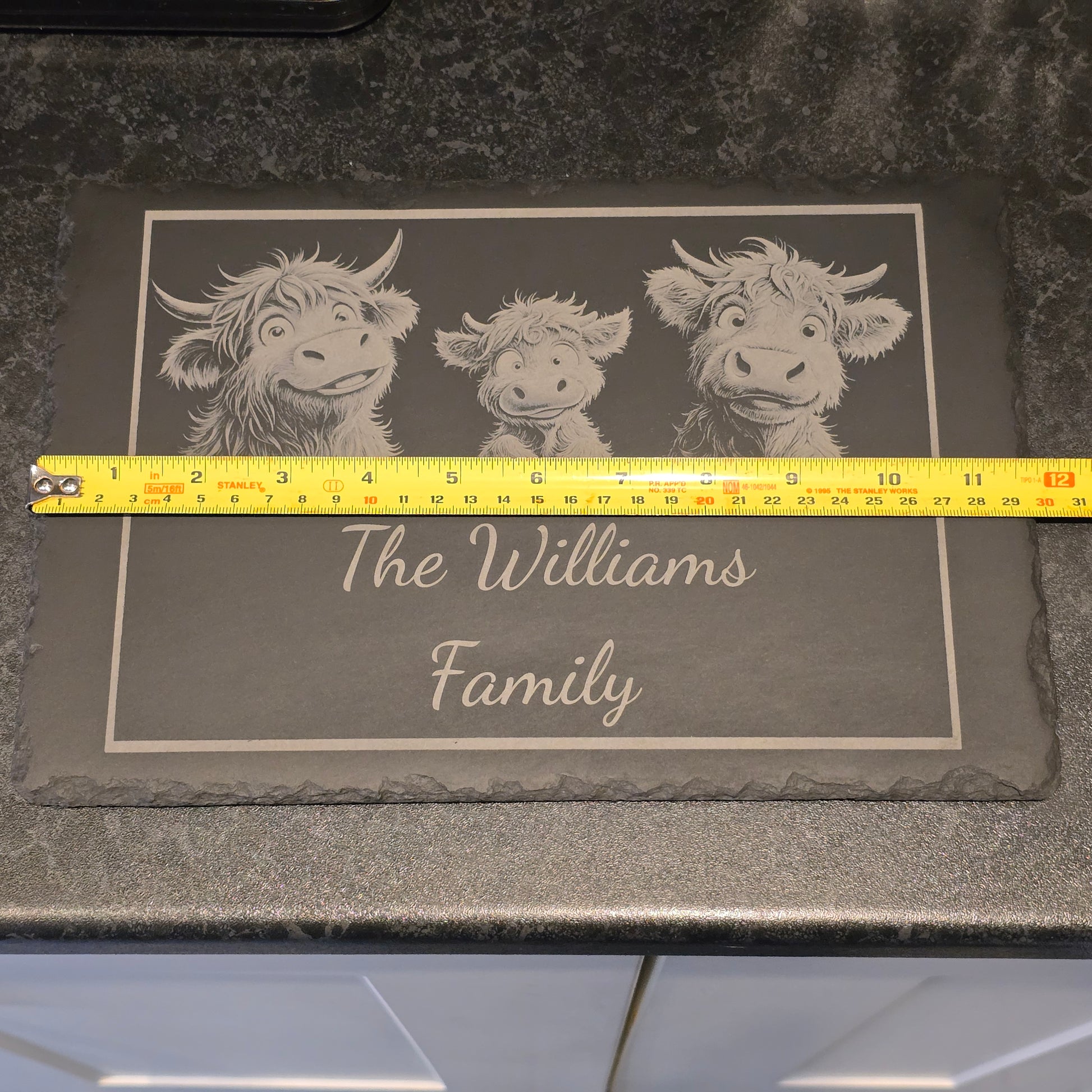 A family of highland cows engraved on a personalised cheese slate measuring 29cm in length