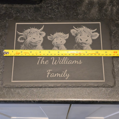 A family of highland cows engraved on a personalised cheese slate measuring 29cm in length