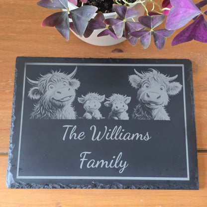 Slate with engraved family of cows and 'The Williams Family' text on a wooden surface with a plant.