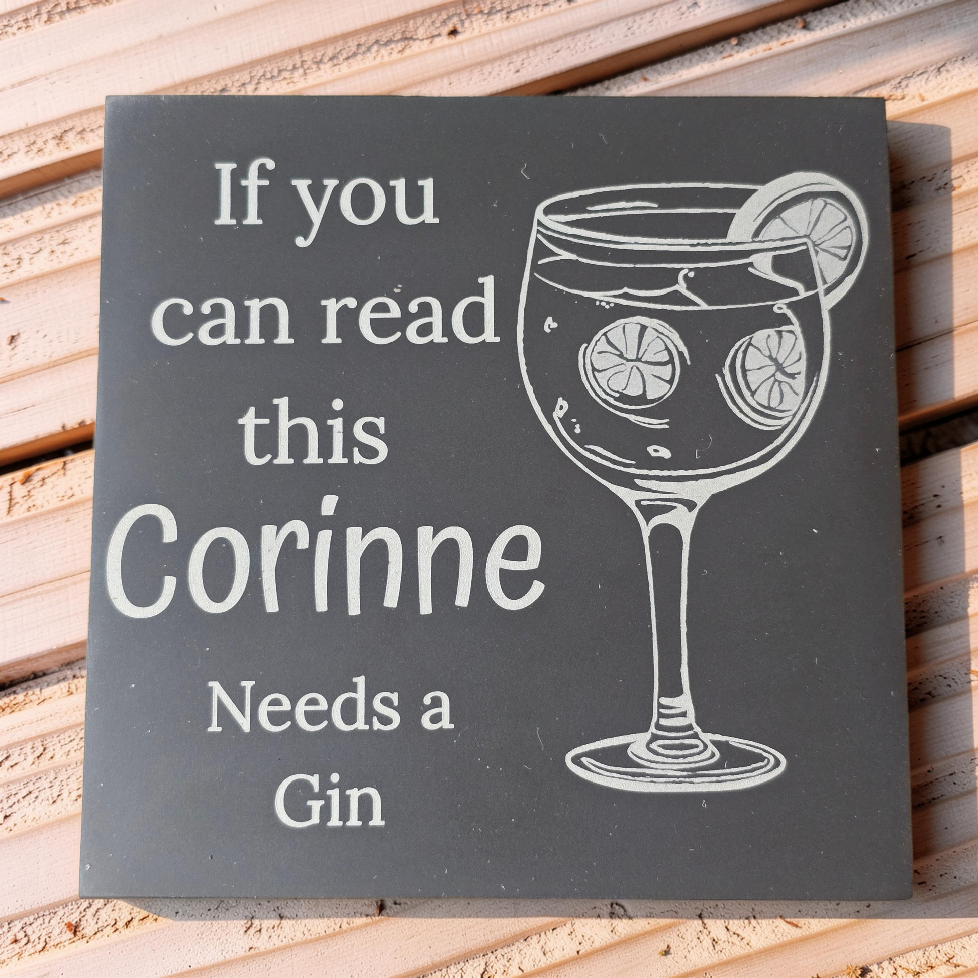 slate coaster with a glass of gin and text engraved a wooden table