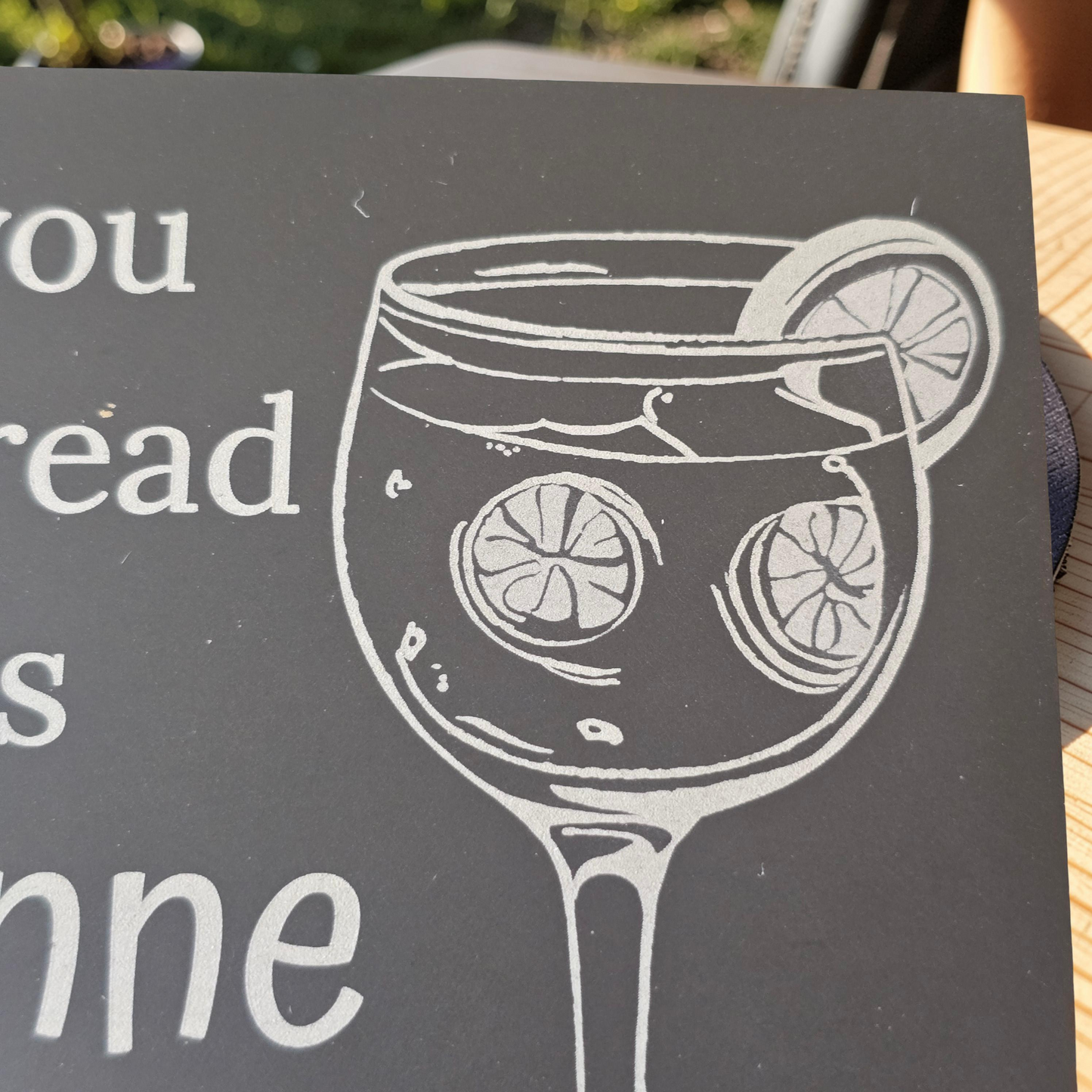 slate coaster with engraving of a glass with lemon slices and text.