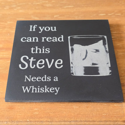 Slate coaster with a glass of whiskey and text 'If you can read this, Steve Needs a Whiskey' on a wooden surface.