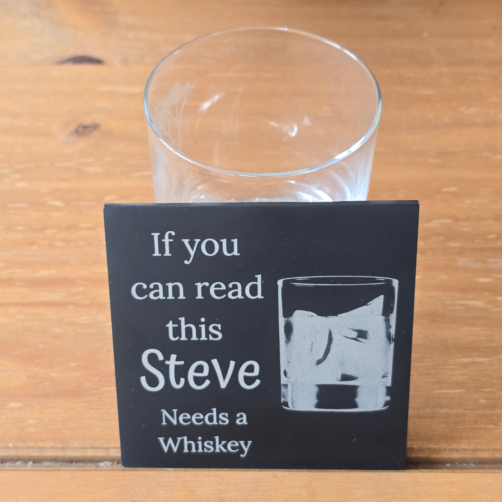 Coaster with text 'If you can read this Steve Needs a Whiskey' on a wooden table