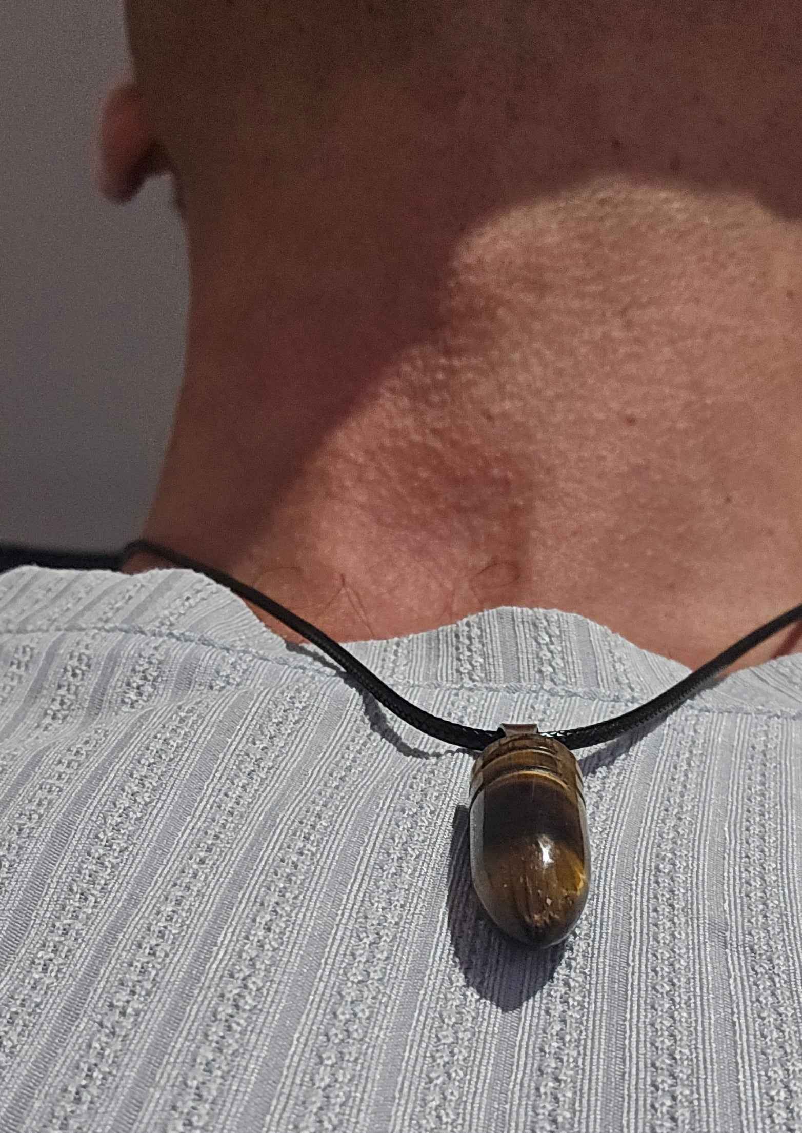 Men's tigers eye stone necklace in a bullet shape being worn around the neck