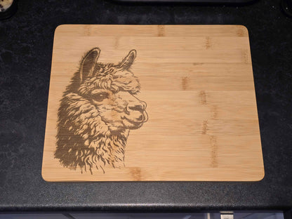 Bamboo cutting board with a laser-engraved alpaca design on a black countertop.