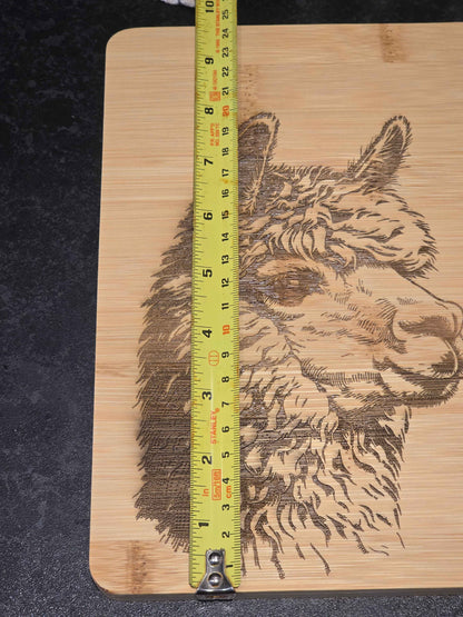 Wooden cutting board with a engraved alpaca design and a tape measure for scale, displaying 24cm width