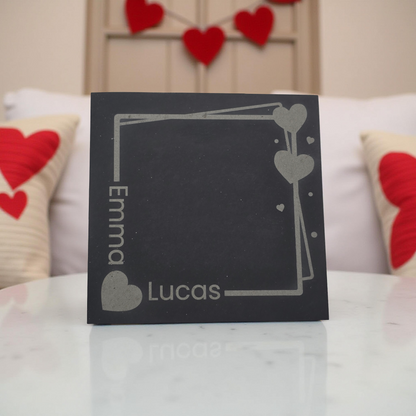 Personalised slate coaster with 'Emma' and 'Lucas' on a surface with heart-themed décor.