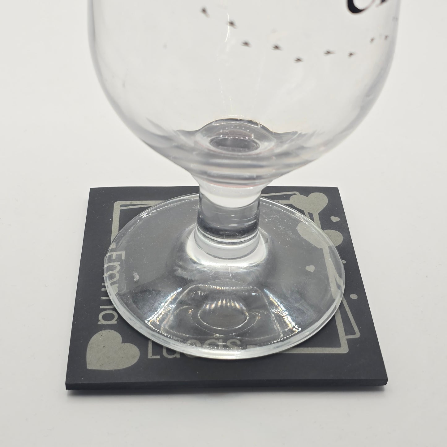 Clear glass sitting on a customised slate coaster featuring 2 names and a framed heart design 